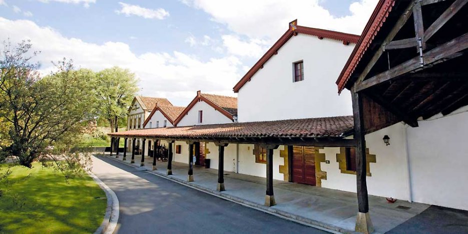 Cune winery in Haro, classic Spanish Riojan building with low red clay tiled roofs, a lean-to held up by rough hewn dark wood pillars, and red painted roof edges