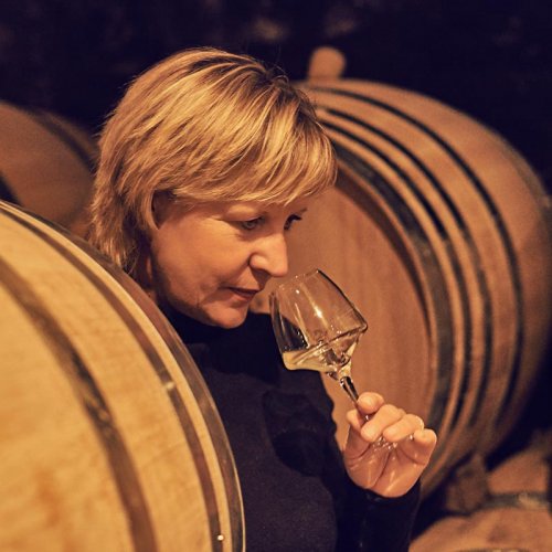 Catherine Corbeau-Mellot, stands in the yellow light of the barrel cellar, and samples from a white wine glass