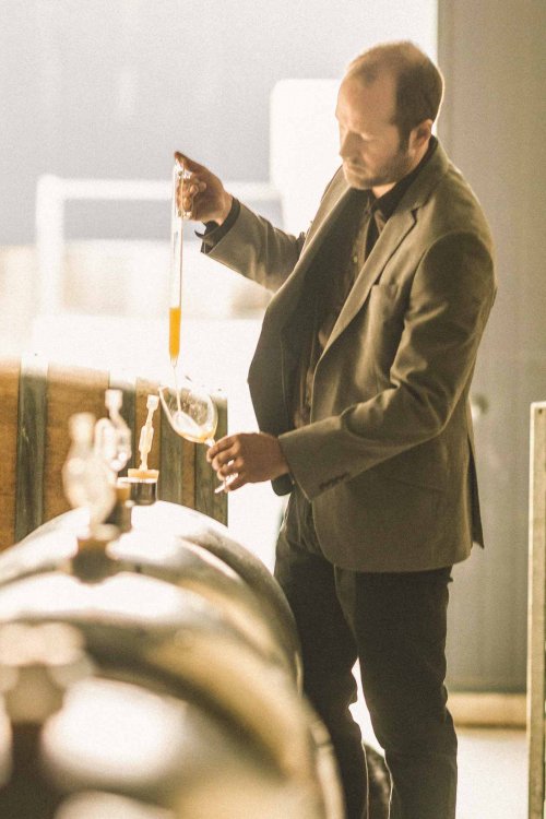 Richard Painter, Winemaker, smartly dressed in jacket, while sampling the progress of white wines from barrels within the sunlit winery