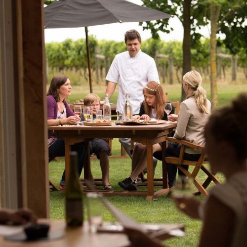 A dining family sit at an outdoor wooden table of the Hawkes Bay winery restaurant