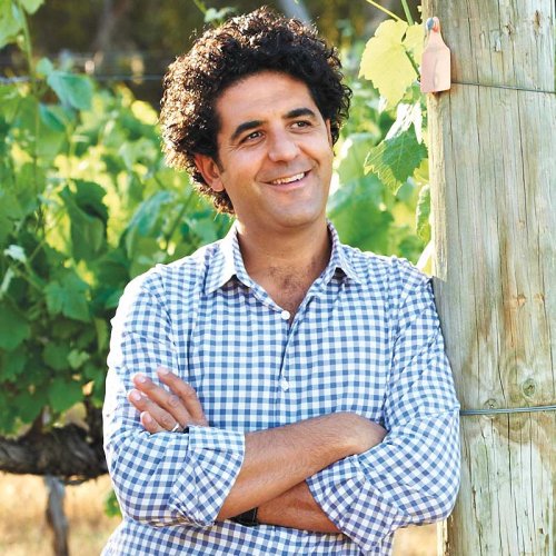 Larry Cherubino, Director of Winemaking, in a blue and white checked shirt, leans against a vine post