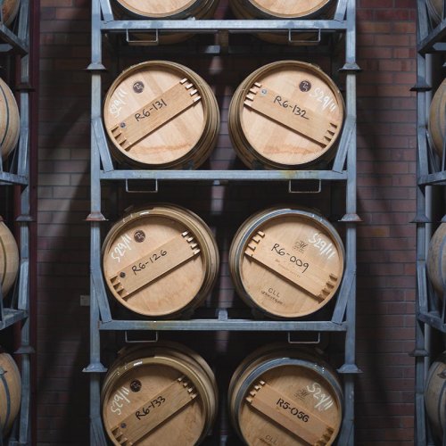 Robert Oatley wines ageing in oak barrels stacked on metal racks against a red brick wall