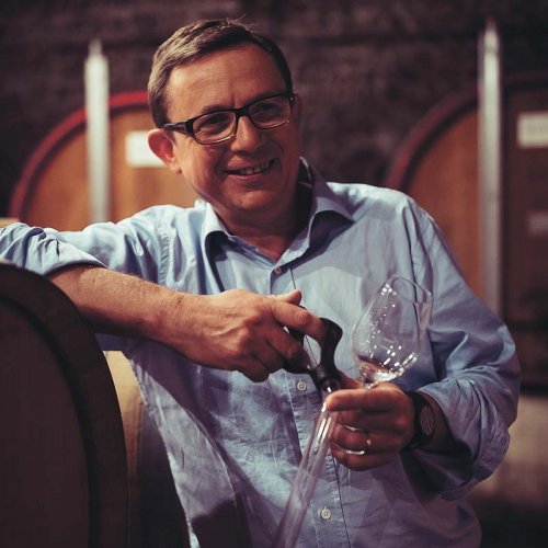 Frédéric Maignet, Consultant Oenologist leaning against a wine barrel in the cellars, midway through sampling the progress of the wine aging