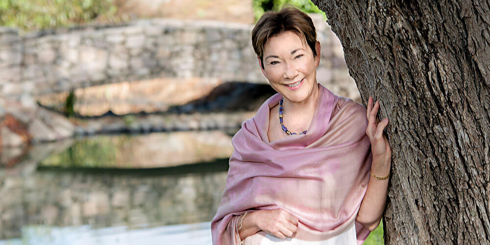 Eileen Crane - Founding Winemaker and President - draped in a pale purple shawl, while leaning on a tree in the gardens of Domaine Carneros