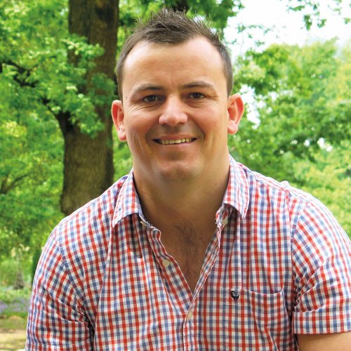 RJ Botha - Winemaker - sitting outside wearing a red, white and blue checked short sleeve shirt