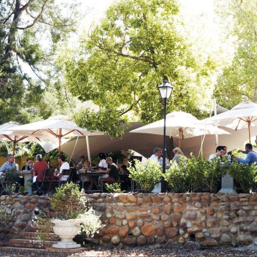 Kleine Zalze's outdoor terrace dining area, full of diners shaded from the sun under large cream parasols