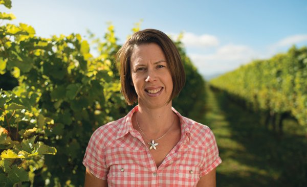Helen Morrison - Senior Marlborough Winemaker - in a pink & white checked shirt stood among the vines