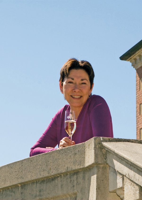 Eileen Crane, leaning against the terrace balustrade with a glass of Brut