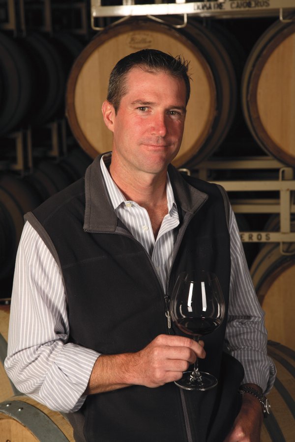 TJ Evans - Pinot Noir Winemaker, wearing a brown gilet in the winery among the barrels