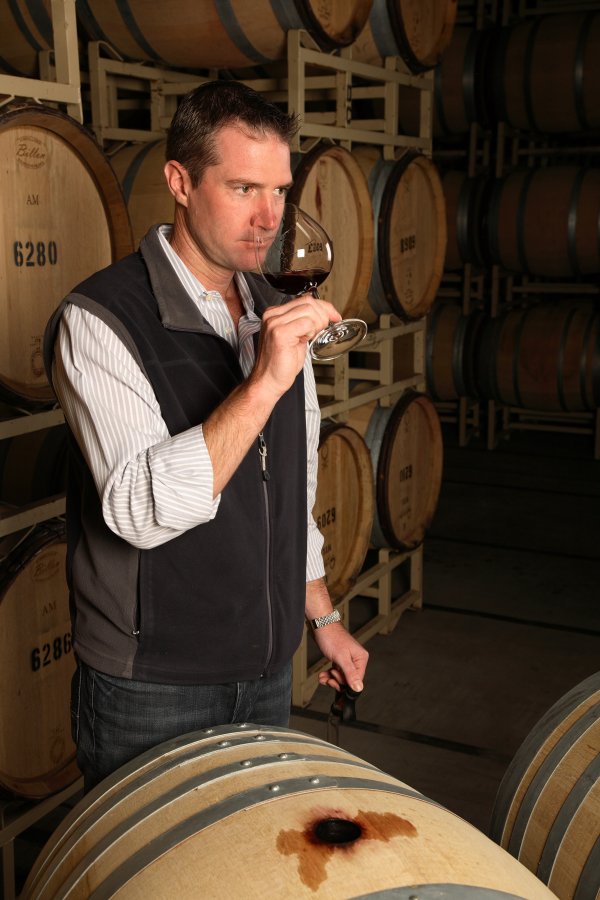 TJ Evans - Pinot Noir Winemaker, wearing a brown gilet in the winery among the barrels, sampling a glass of Pinot Noir