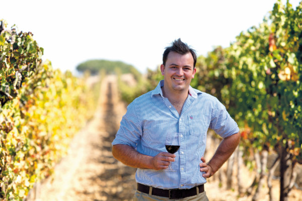 RJ Botha - Winemaker - in the vineyard, wearing a blue striped shirt, holding a glass of red wine