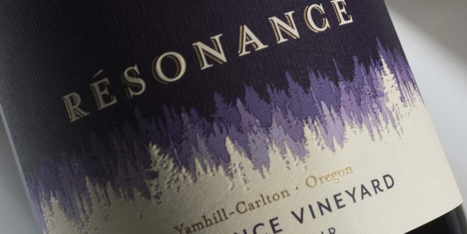 Close up of the Resonance bottle label in purple and cream. The design is of rows of pine like trees that seem to disappear to the distance, the lightest are cream coloured like the foreground which has the wine details printed in a modern type style on, and as the rows of trees seemingly go into the distance, their colours change from the cream to a light purple, then a mid purple to the dark purple at the top of the label.