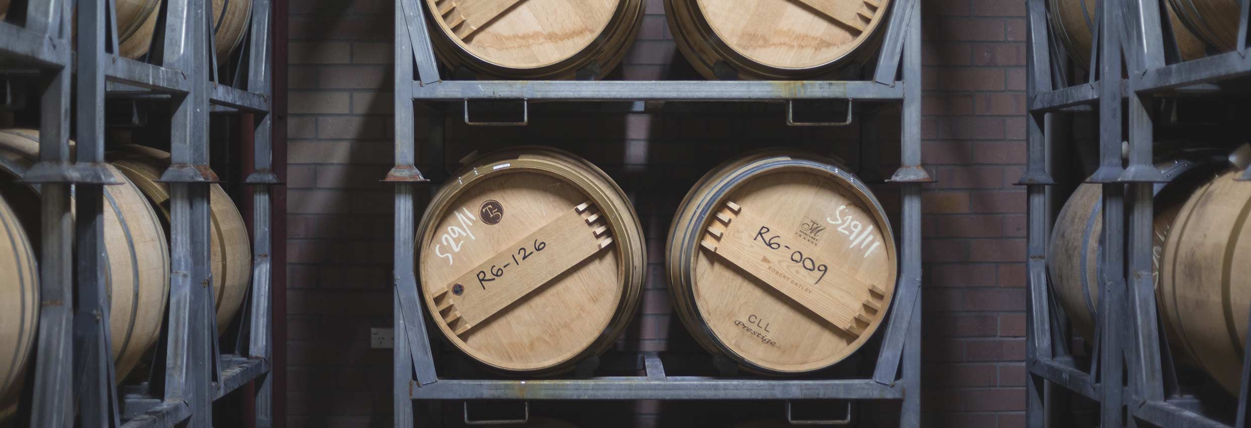 view of barrel ends with handwritten notes in letters and numbers, sitting on a grey steel rack of shelves in front of a red brick wal